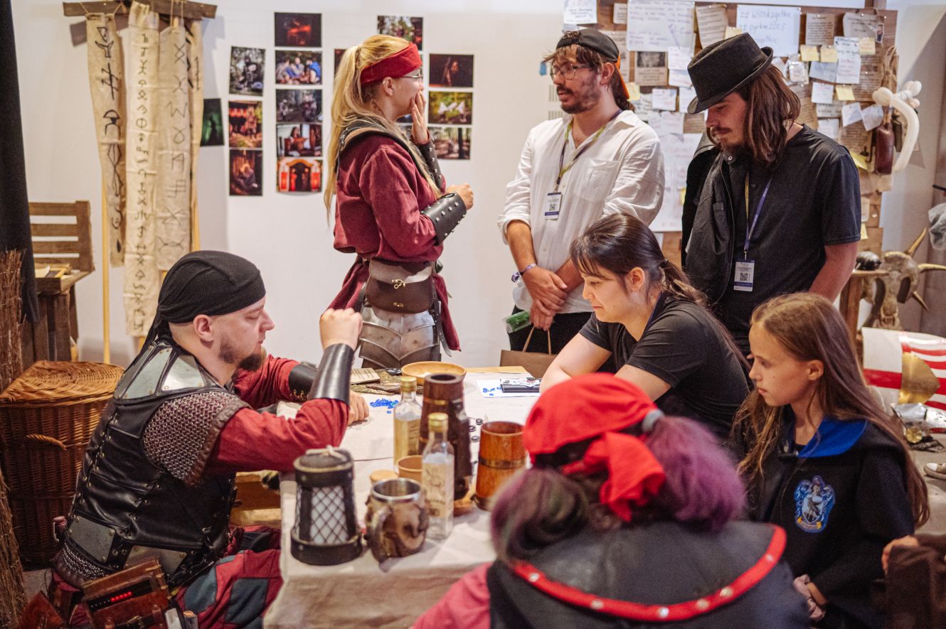 Grupa ludzi w cosplayu siedzi przy stole i rozmawia.