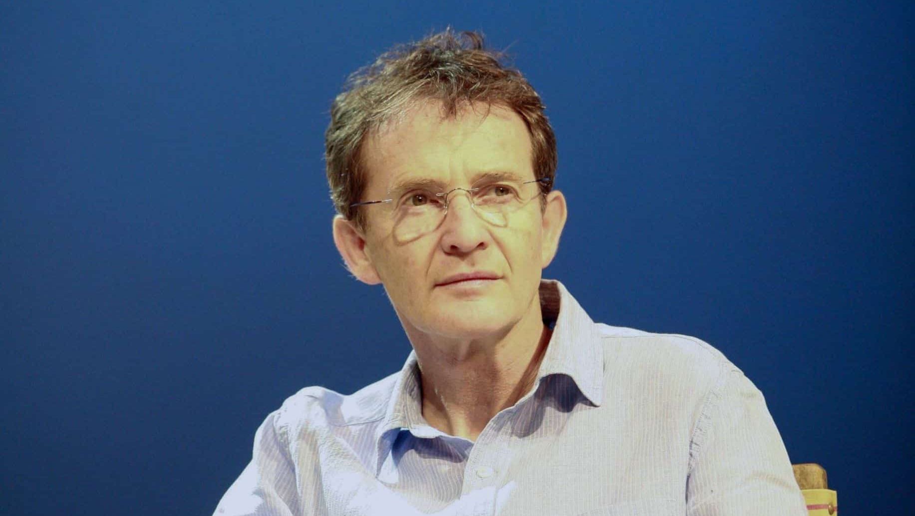 Anton Lesser siedzi na krześle z głową skręconą lekko w lewo