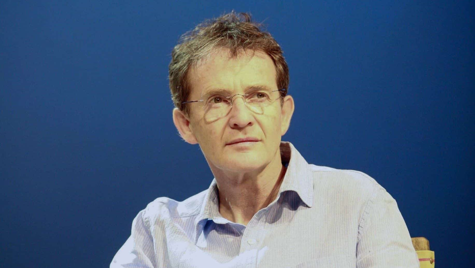 Anton Lesser siedzi na krześle z głową skręconą lekko w lewo